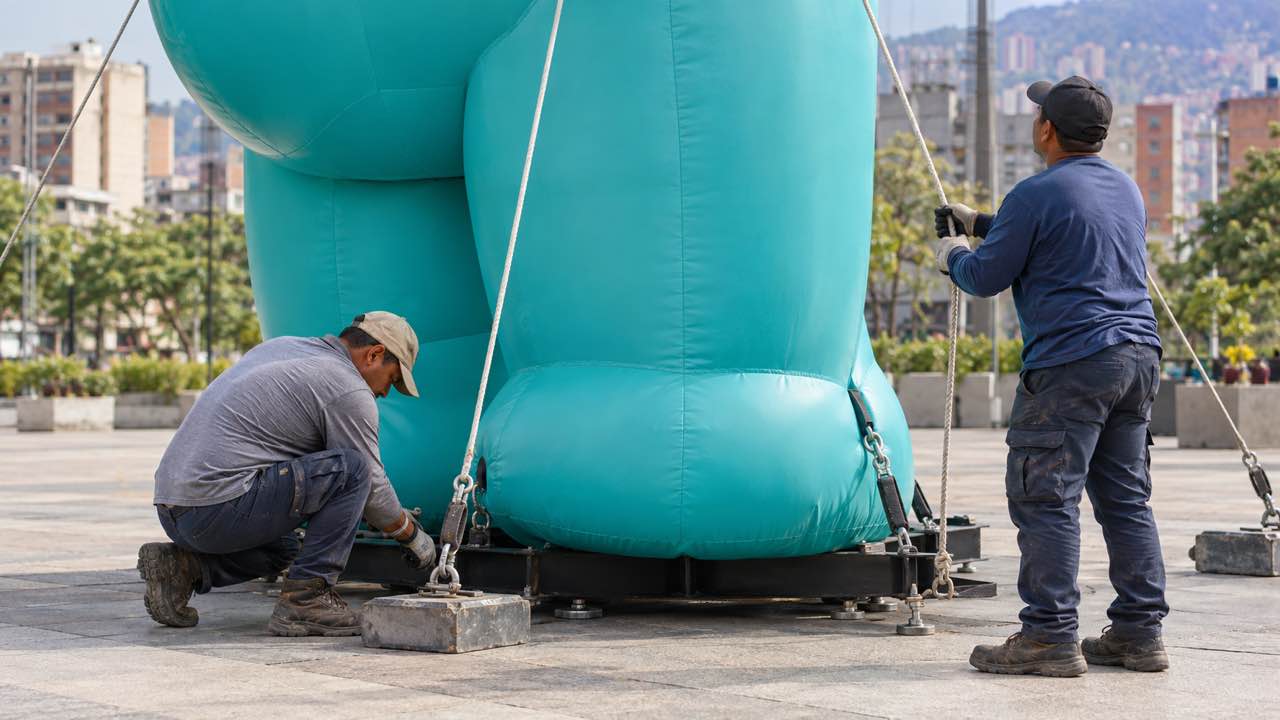 Equipo instala un dummy inflable publicitario sujeto a una base en un espacio exterior urbano.